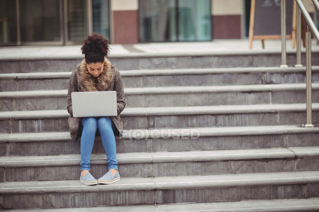 Повна довжина жінки, використовуючи ноутбук, сидячи на кроках — стокове фото