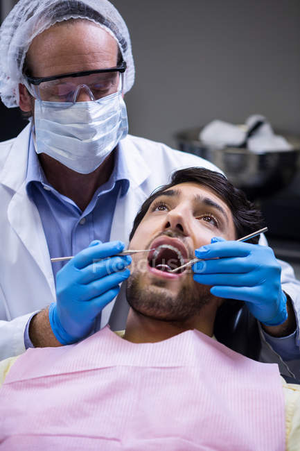 Dentista examinando a un paciente con herramientas en la clínica dental - foto de stock