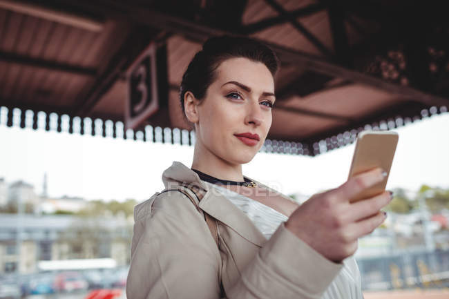 Mujer joven sosteniendo teléfono móvil en la estación de tren - foto de stock