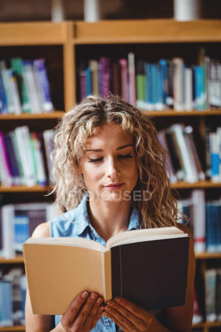 Bella donna che legge libro in biblioteca — Foto stock
