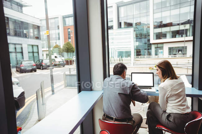 Vue arrière de l'homme et de la femme discutant sur ordinateur portable à la cafétéria — Photo de stock