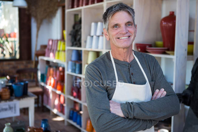 Щасливий чоловічий гончар стоїть з обіймами, схрещеними в керамічній майстерні — стокове фото