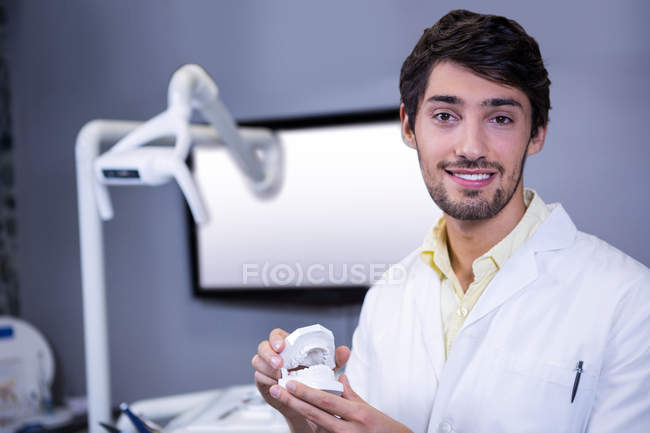 Dentista sorridente segurando um modelo de boca na clínica odontológica — Fotografia de Stock