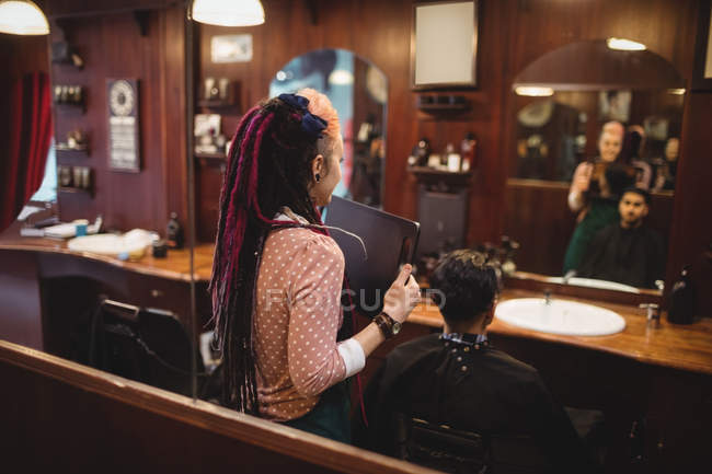 Femme barbier montrant homme sa coupe de cheveux dans le miroir au salon de coiffure — Photo de stock