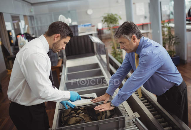 Oficial de seguridad del aeropuerto usando un detector de metales para revisar una bolsa en el aeropuerto - foto de stock