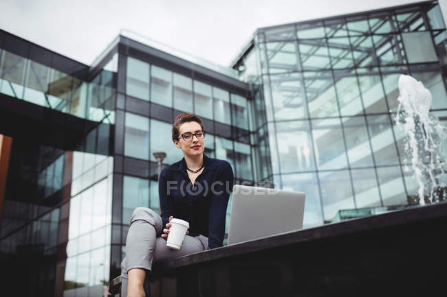 Jovem empresária sentada contra prédio de escritórios moderno — Fotografia de Stock
