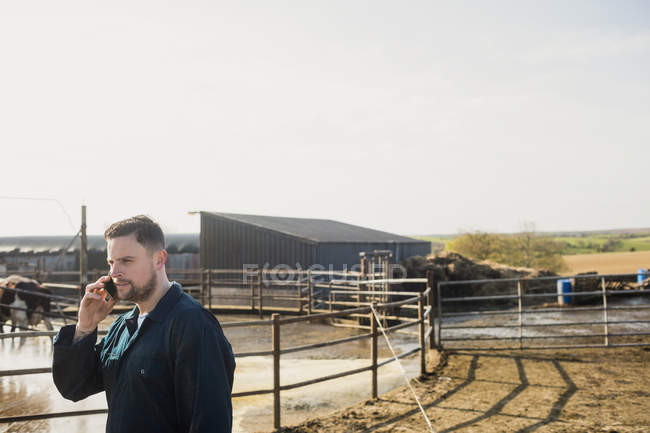 Працівник ферми розмовляє на мобільному телефоні, стоячи біля паркану на тлі чистого неба — стокове фото