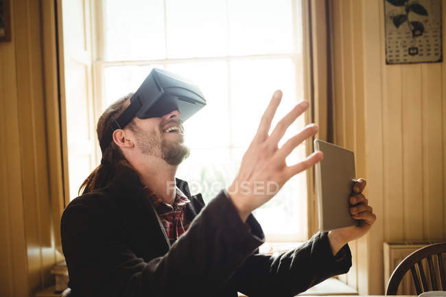 Hipster segurando tablet ao usar simulador de realidade virtual em casa — Fotografia de Stock