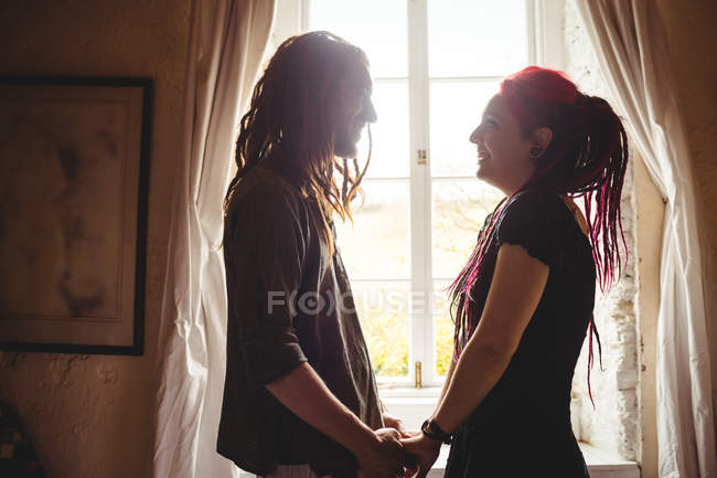 Sorrindo jovem casal de mãos dadas contra janela em casa — Fotografia de Stock