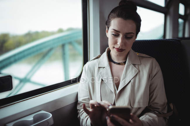 Hermosa mujer usando el teléfono móvil mientras está sentado en el tren - foto de stock