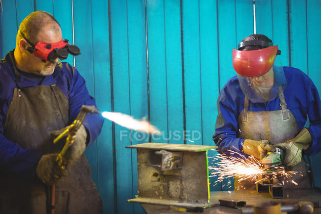 Soudeurs sciant le métal avec des outils de travail électriques et de soudage en atelier — Photo de stock