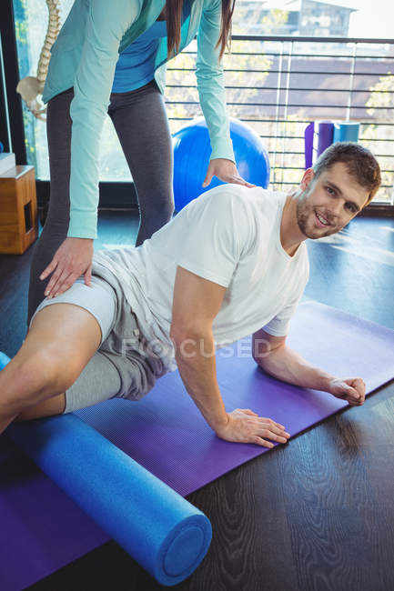 Retrato del fisioterapeuta femenino que da fisioterapia a la rodilla del paciente masculino en la clínica - foto de stock