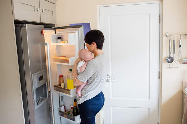 Mutter mit Baby schaut zu Hause in Kühlschrank in Küche — Stockfoto