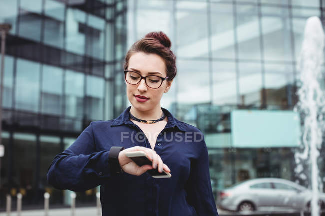 Geschäftsfrau kontrolliert Zeit vor Bürogebäude — Stockfoto