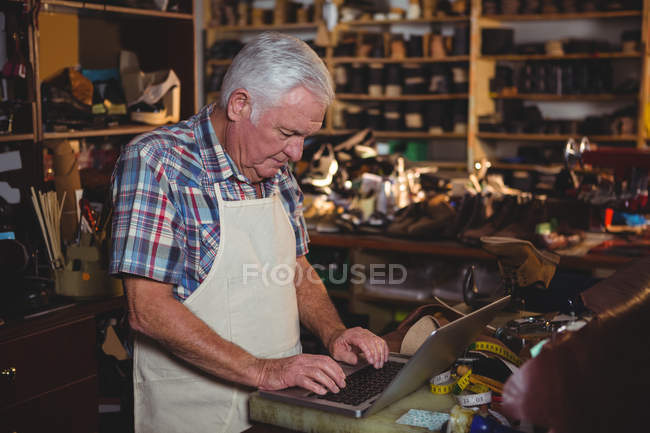 Обувщик с помощью ноутбука в интерьере мастерской — стоковое фото
