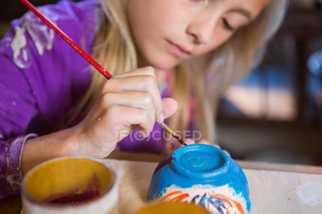 Внимательная девушка рисует на чаше в мастерской по керамике — стоковое фото