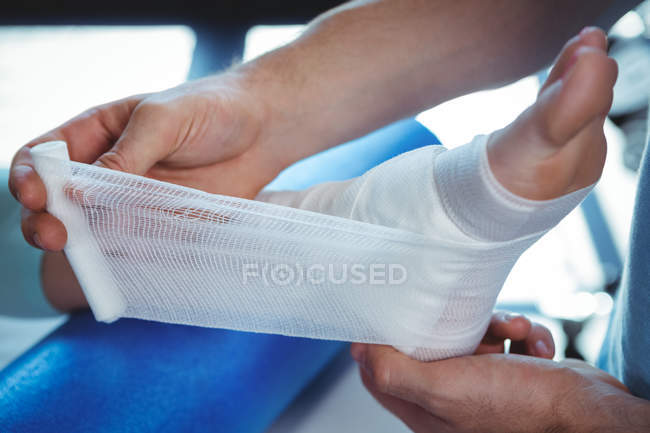 Image recadrée du thérapeute masculin mettant bandage sur le pied du patient féminin en clinique — Photo de stock