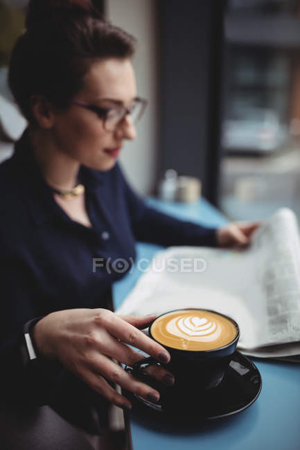 Jeune femme d'affaires avec tasse de café lecture journal dans le café — Photo de stock