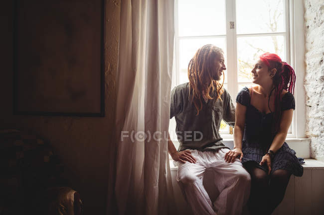 Sonriente joven pareja sentada contra la ventana en casa - foto de stock