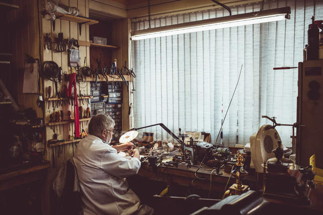 Rückansicht eines Uhrmachers, der in der Werkstatt eine Uhr repariert — Stockfoto