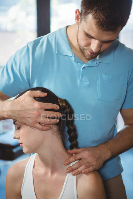 Fisioterapeuta estirando cuello de paciente femenina en clínica - foto de stock