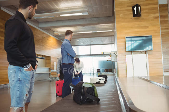 Personas que esperan equipaje en el área de reclamo de equipaje en el aeropuerto - foto de stock