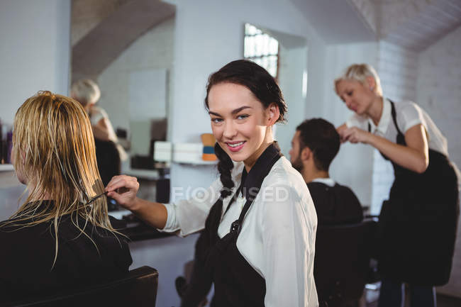 Портрет усміхненого перукаря розчісує клієнтське волосся в салоні — стокове фото