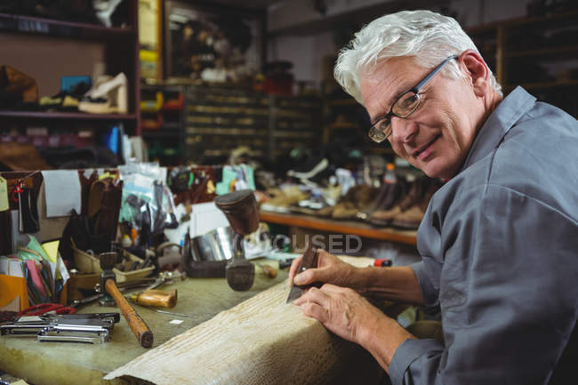 Zapatero senior cortando un trozo de material en el taller - foto de stock