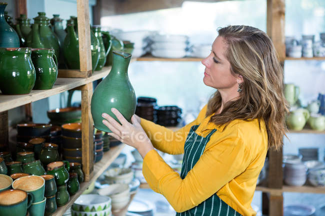 Female potter placing pot on shelf in pottery workshop — Stock Photo