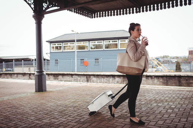 Longitud total de la mujer joven que lleva la maleta en la plataforma de la estación de tren - foto de stock