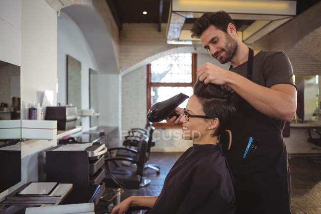 Женщина высушивает волосы феном в парикмахерской — стоковое фото