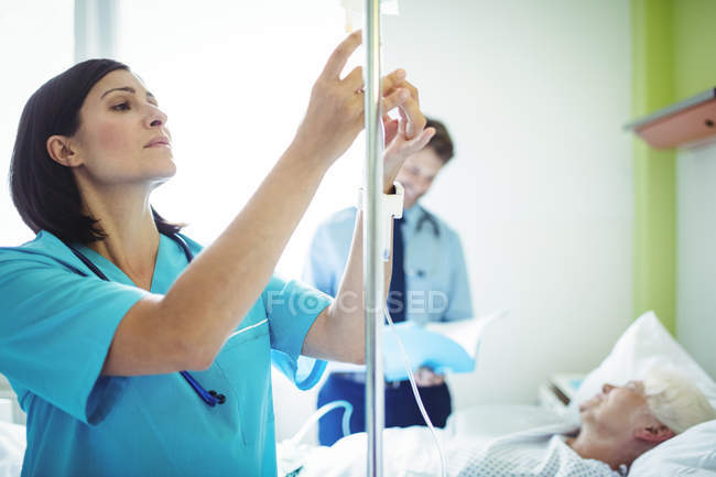 Enfermera revisando un goteo salino en el hospital - foto de stock