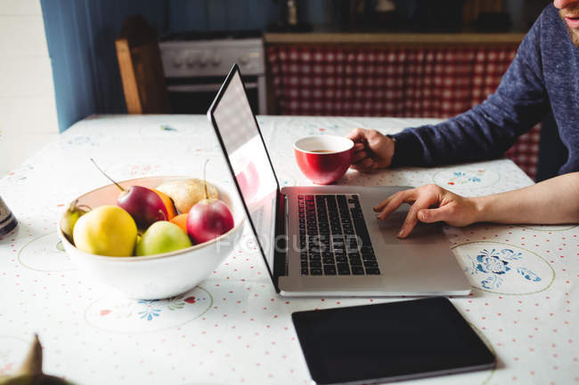 Abgeschnittenes Bild eines Paares mit Laptop, während Obst und digitales Tablet zu Hause auf dem Tisch liegen — Stockfoto