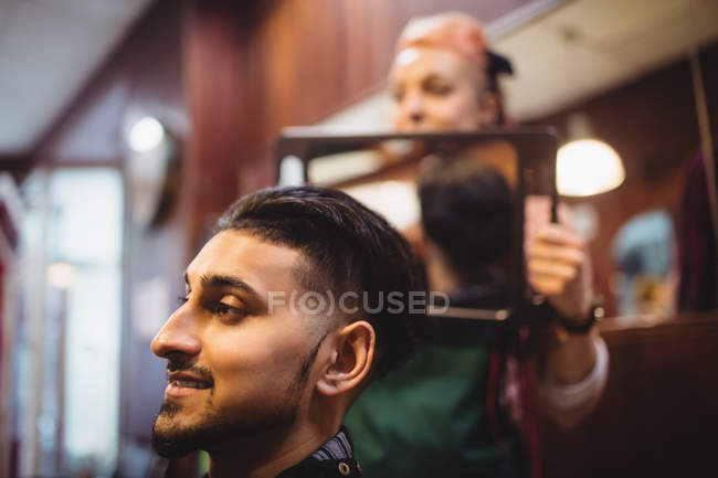 Mulher barbeiro mostrando o homem seu corte de cabelo no espelho na barbearia — Fotografia de Stock