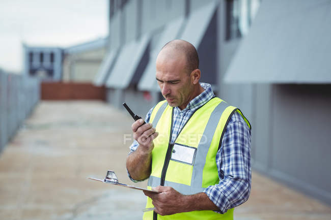 Travailleur de la construction parlant sur walkie-talkie devant le bureau — Photo de stock