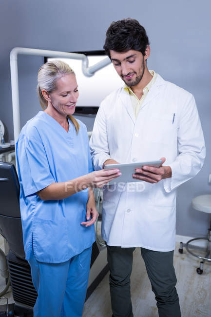 Dentista y asistente dental trabajando junto con la tableta en la clínica dental - foto de stock