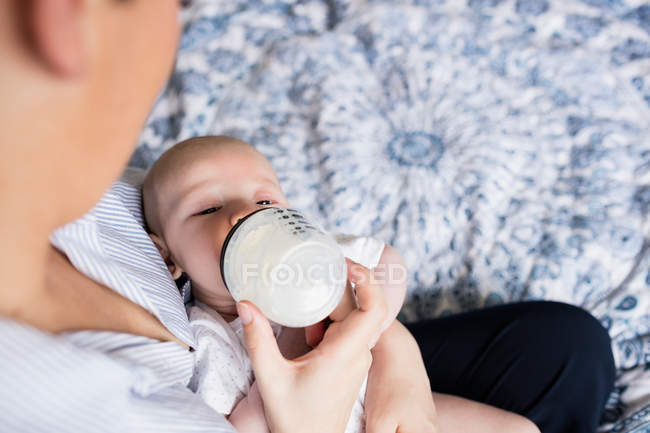 Image recadrée de mère nourrissant bébé avec du biberon dans la chambre à coucher à la maison — Photo de stock