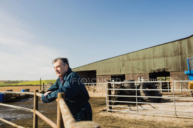 Operaio agricolo appoggiato sulla recinzione al fienile contro il cielo — Foto stock