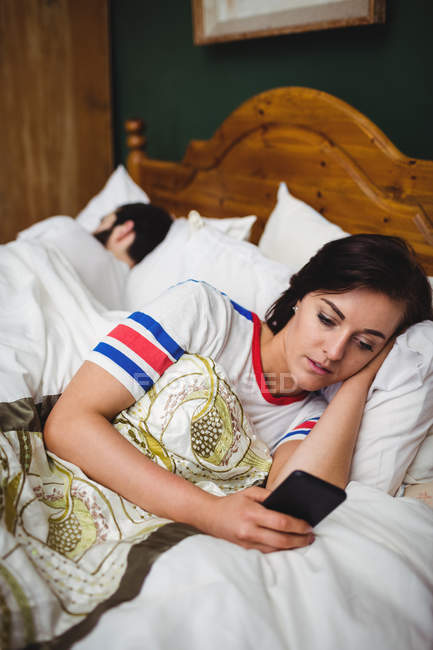 Женщина с мобильным телефоном, лежащая на кровати в спальне — стоковое фото