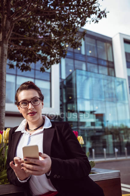 Young businesswoman holding mobile phone against office building — Stock Photo