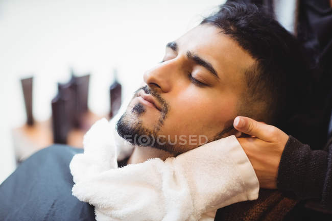 Barbeiro aplicando uma toalha quente em um rosto de cliente na barbearia — Fotografia de Stock