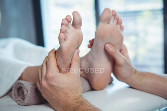 Обрезанное изображение мужского физиотерапевта, делающего массаж ступней пациентке в клинике — стоковое фото