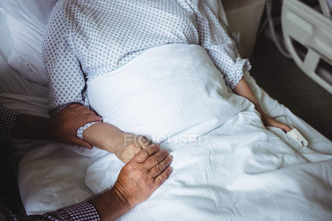 Обрезанный вид пожилого мужчины, держащегося за руки пожилой женщины в больнице — стоковое фото