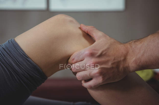 Immagine ritagliata del fisioterapista che somministra fisioterapia al ginocchio della paziente in clinica — Foto stock