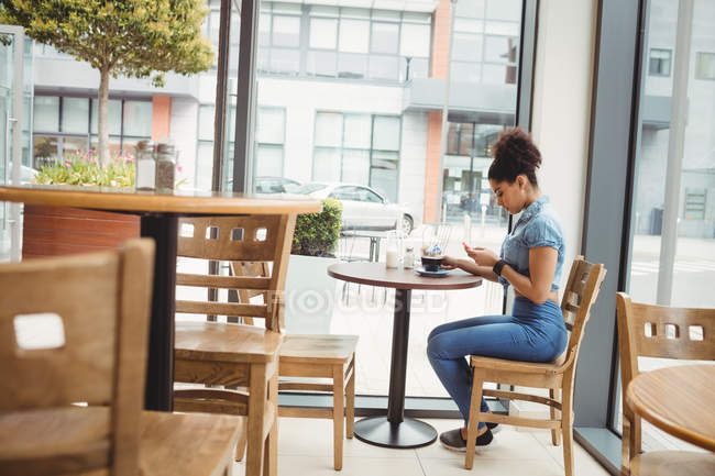 Повна довжина жінки, використовуючи телефон, сидячи в ресторані — стокове фото