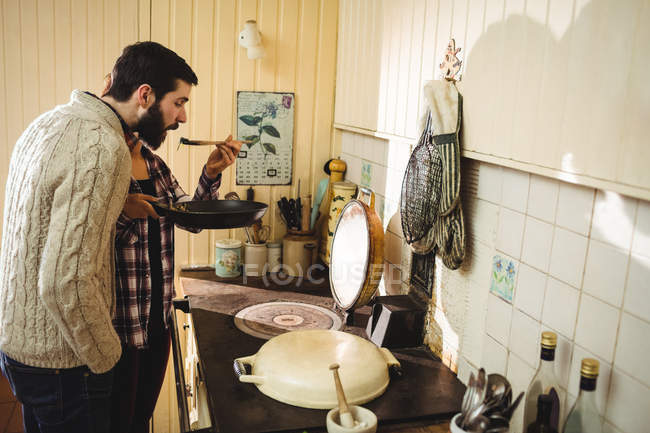 Чоловік дегустує їжу, приготовану жінкою на кухні — стокове фото