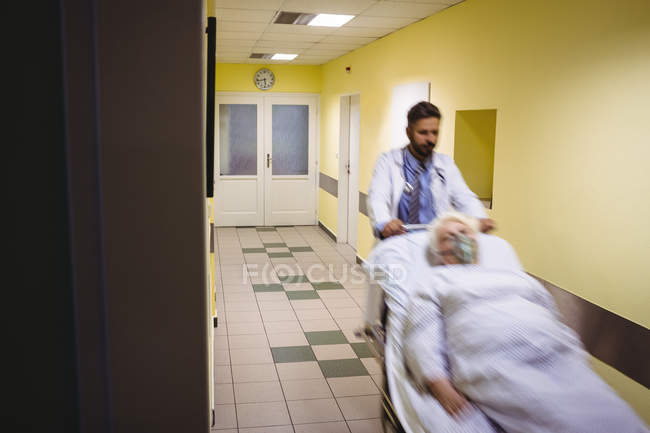 Размытый взгляд на то, как доктор толкает пожилого пациента на носилки в коридоре больницы — стоковое фото