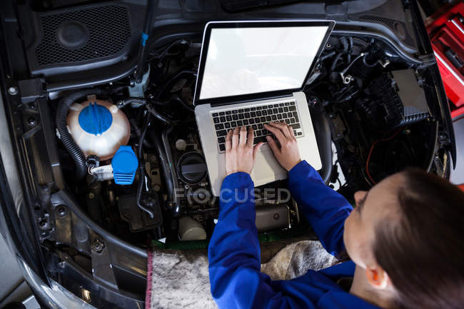 Meccanico femminile che utilizza un tablet digitale durante la manutenzione del motore dell'auto presso il garage di riparazione — Foto stock