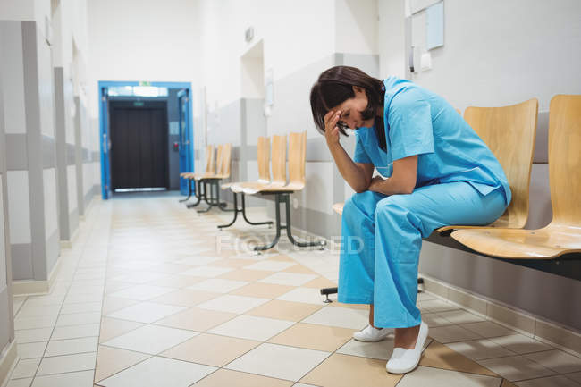 Сумно медсестра, сидячи на дерев'яні стільці в лікарні коридор — стокове фото