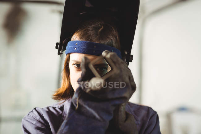 Female welder looking through piece of metal in workshop — Stock Photo